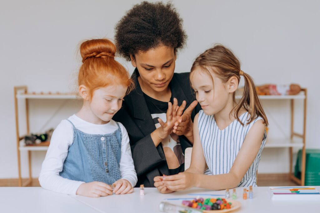 A teacher with two students, one on each side, helping the students count figurines. 