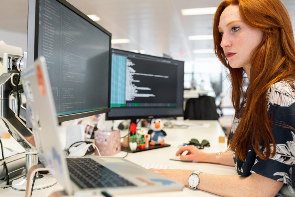 A young woman coding on three computer screens. 